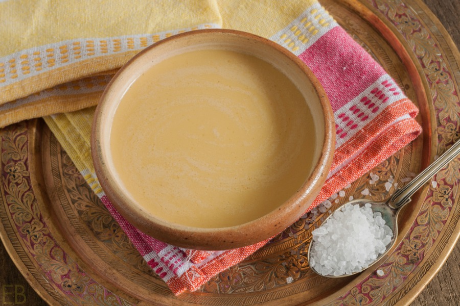 a bowl of tibetan yak butter tea on a red and yellow towel with a spoon of mineral salt nearby