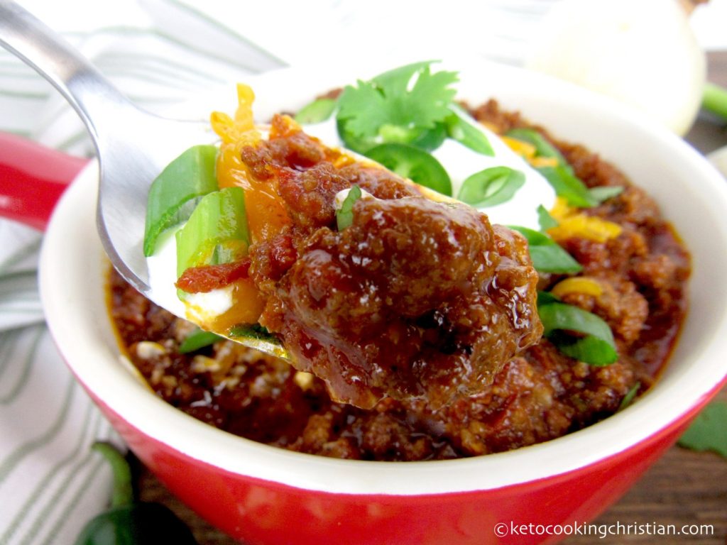 a spoonful of no bean chili that's keto for super bowl party meal served in red bowl with cheese and other toppings