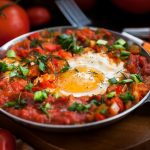 one pan of shakshuka and eggs surrounded by fresh tomatoes