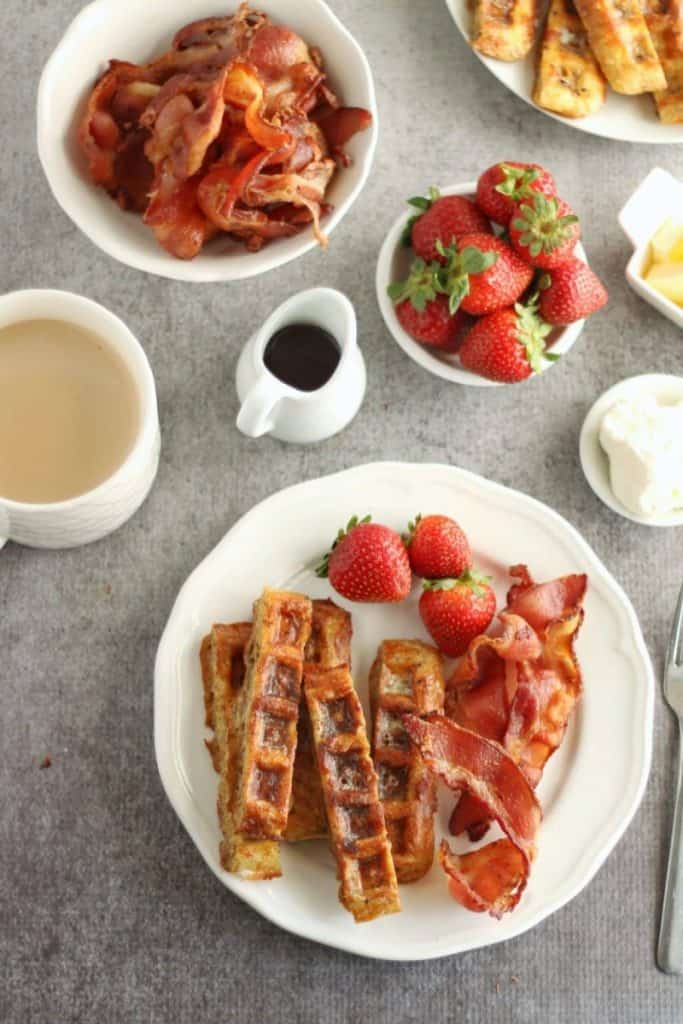 chaffle french toast sticks on white plates with fresh strawberries