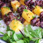 broiled thai beef kabobs on rice in white bowl with mint