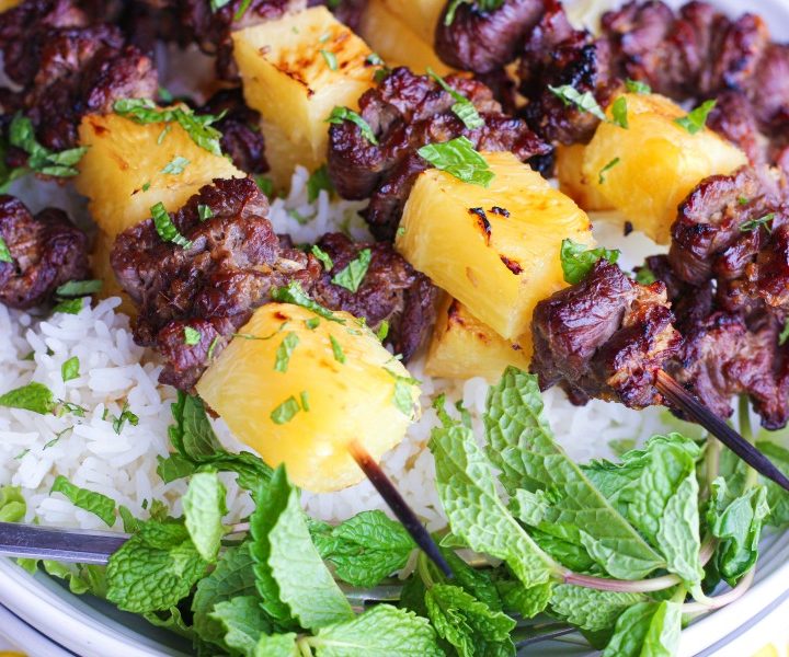 broiled thai beef kabobs on rice in white bowl with mint