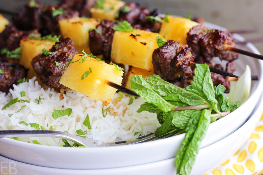 fresh pineapple and beef kabobs on white rice with fresh mint in white bowl