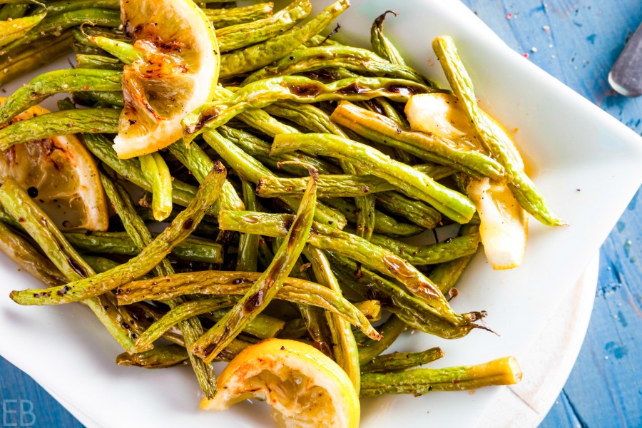 white dish of roasted green beans with lemon slices