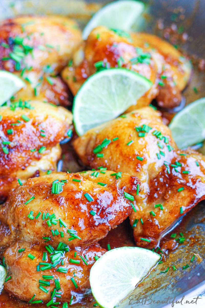 spicy honey lime chicken thighs with lime wedges in cooking pan