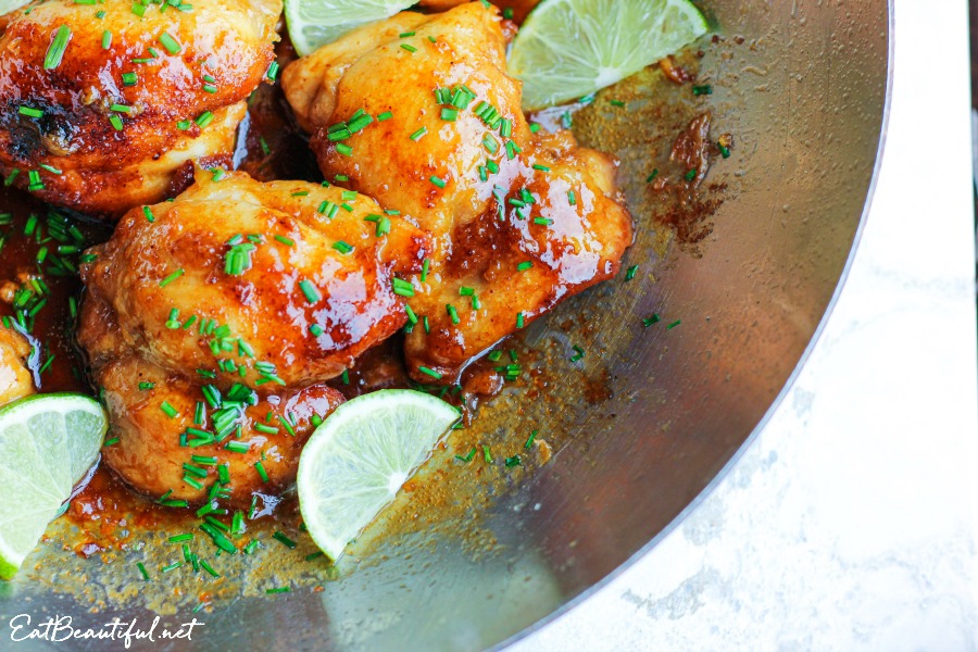 corner view of pan with spicy honey lime chicken thighs with chives and lime slices