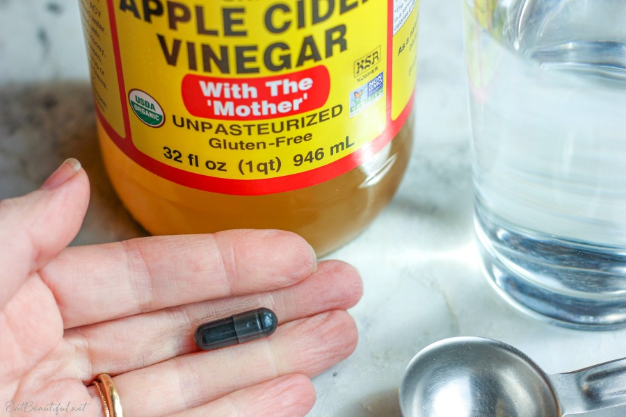 a hand holding one capsule of activated charcoal with ACV in the background