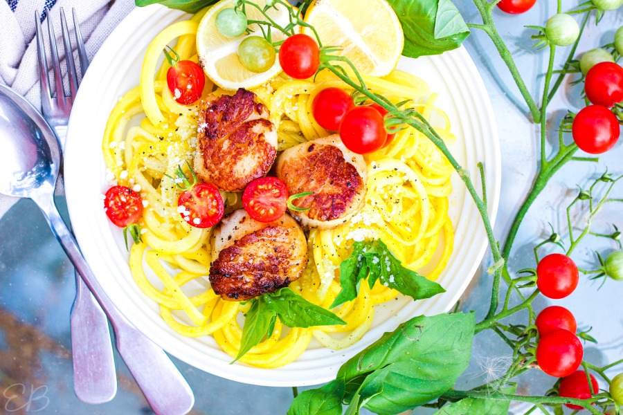 aerial view of scallop scampi with zucchini noodles and fresh basil leaves in white plate