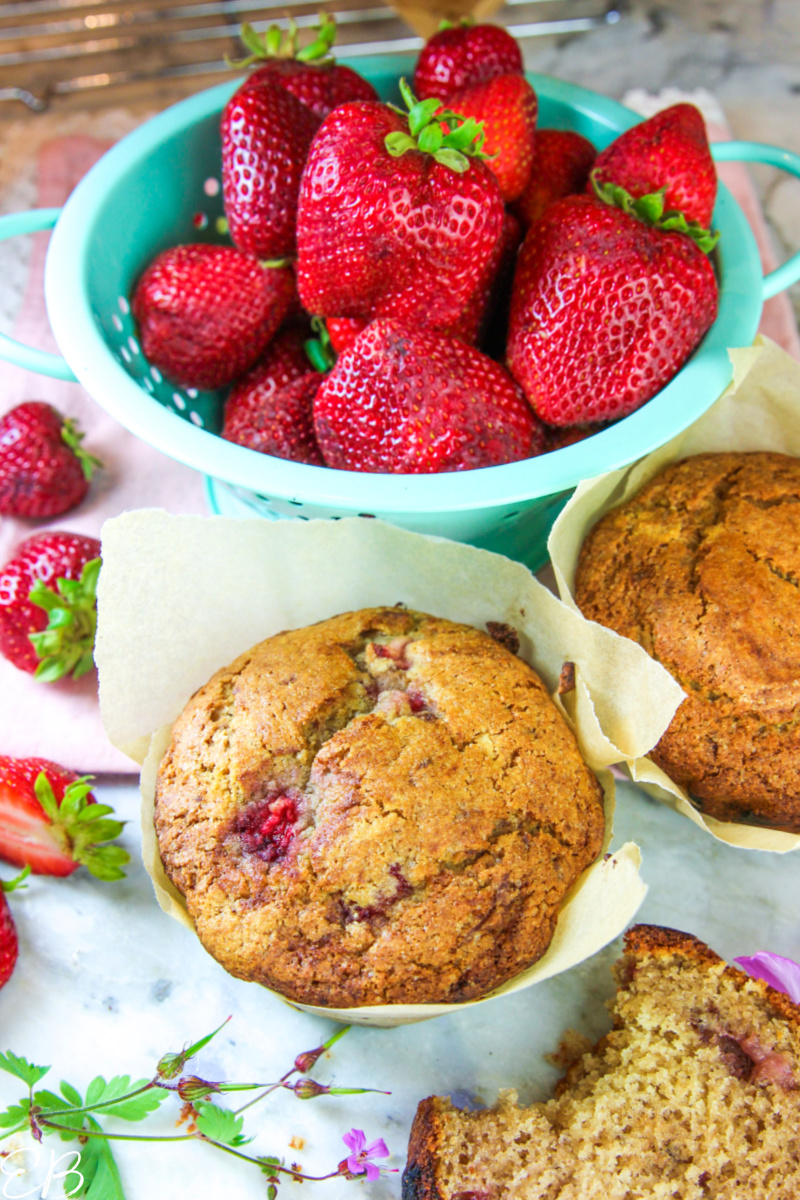 a colander full of fresh strawberries and 3 muffins