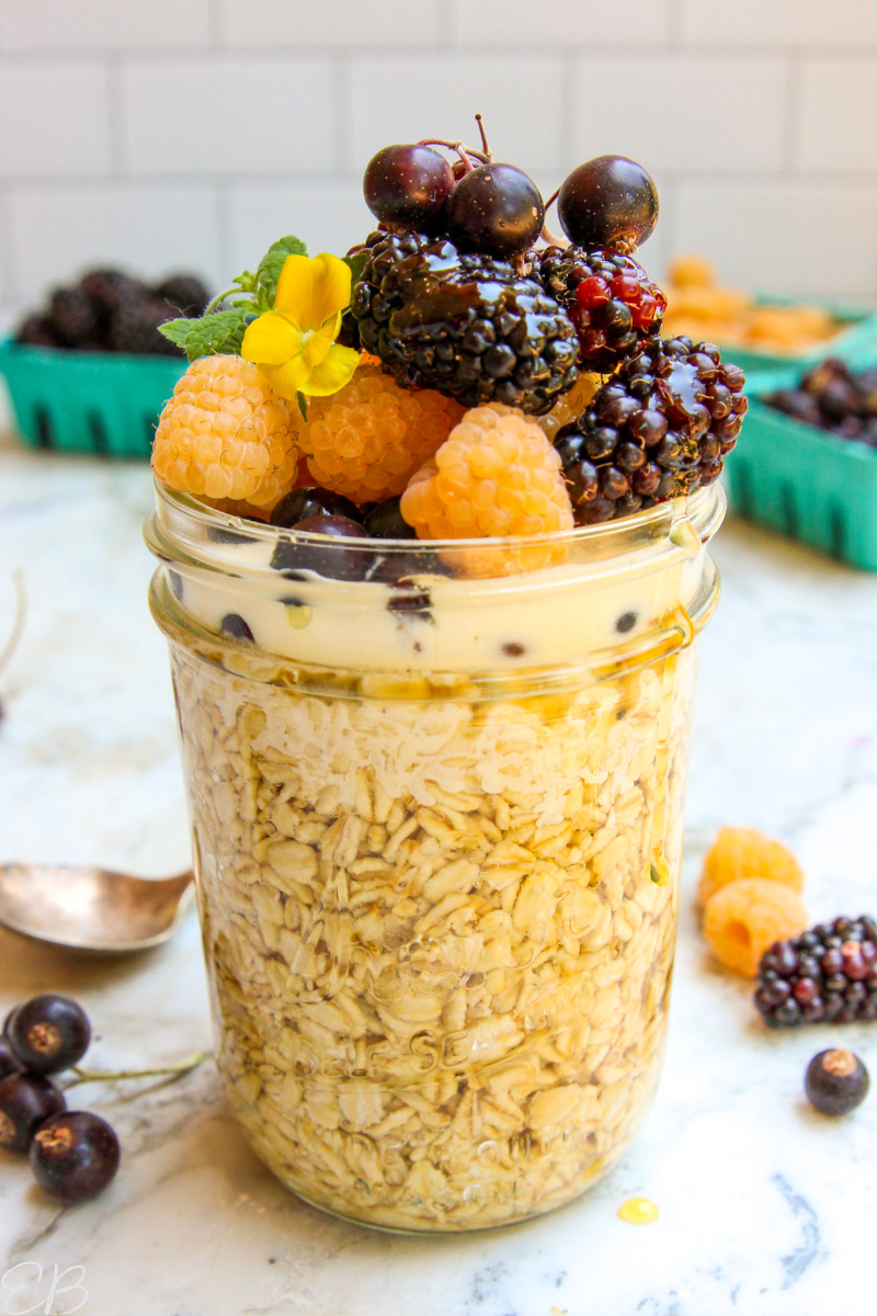 a jar of overnight oats topped high with toppings of fresh berries, cream and honey