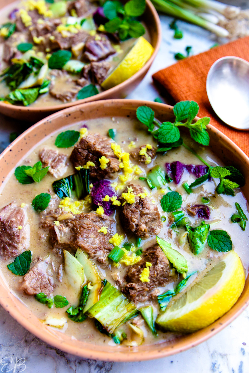 vertical photo of Low-FODMAP beef curry in rustic bowls with toppings of herbs and lemon