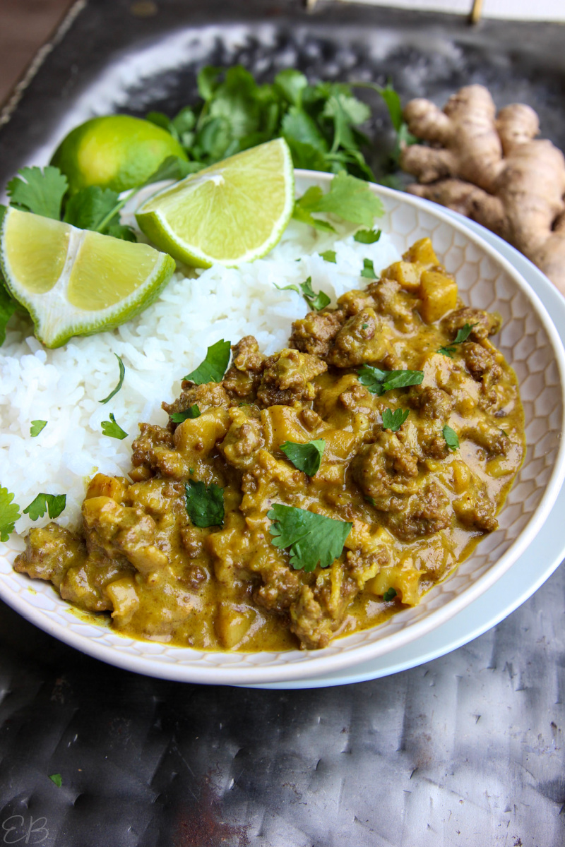 side angle view of ground beef curry on white plate with white rice and limes