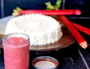 rhubarb sauce in jar in front of cake and stalks of rhubarb