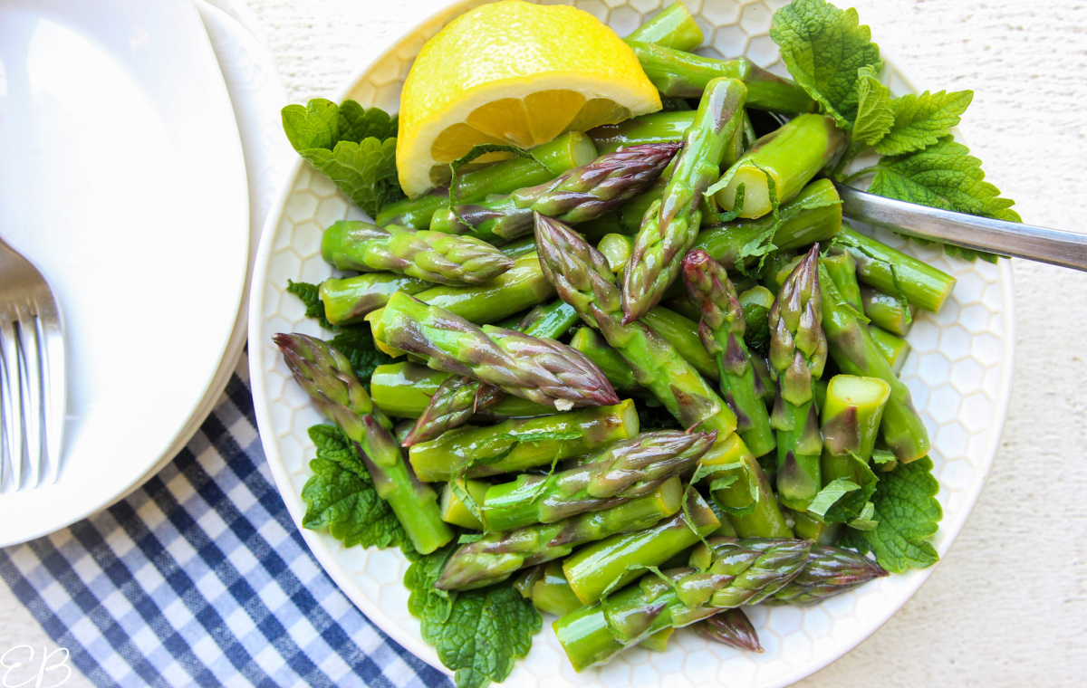OVERHEAD VIEW OF MARINATED ASPARAGUS SALAD IN WHITE BOWL WITH LEMON