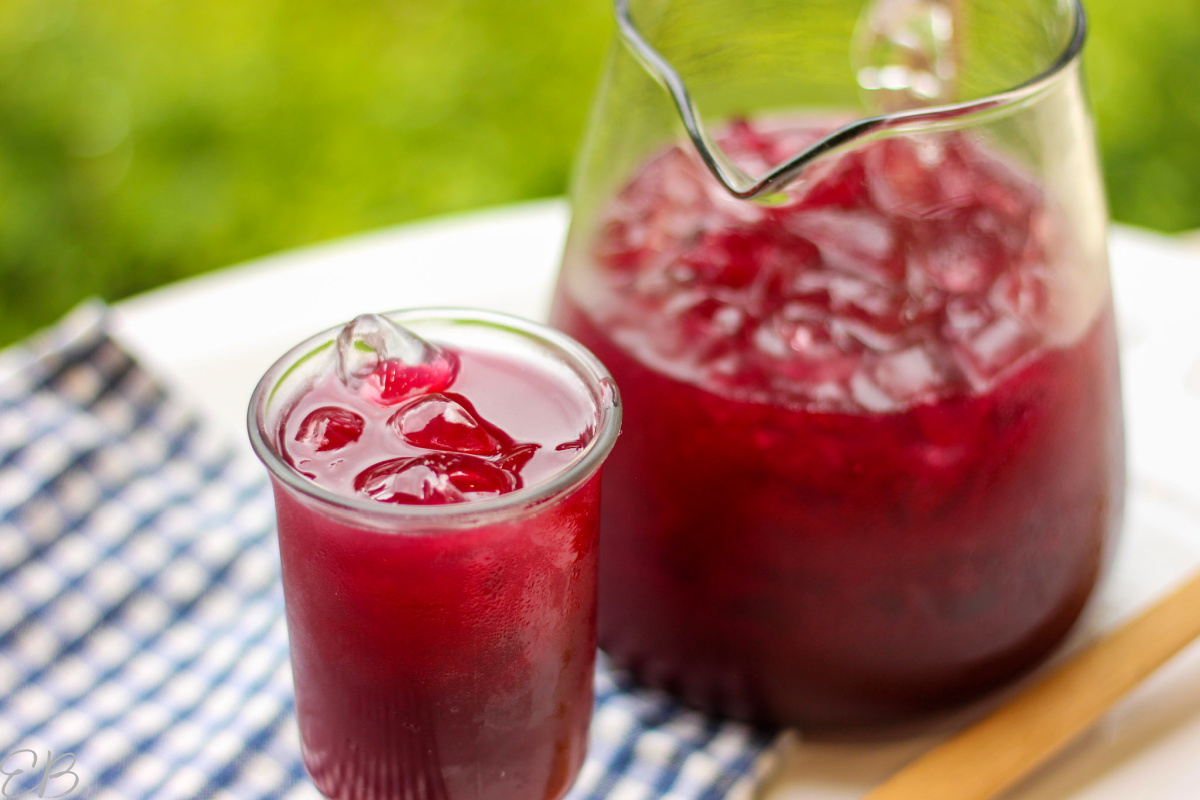 glass of blueberry switchel in the foreground and pitcher in the background