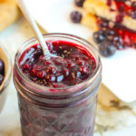 spoon in blueberry jam jar with sandwich in the background