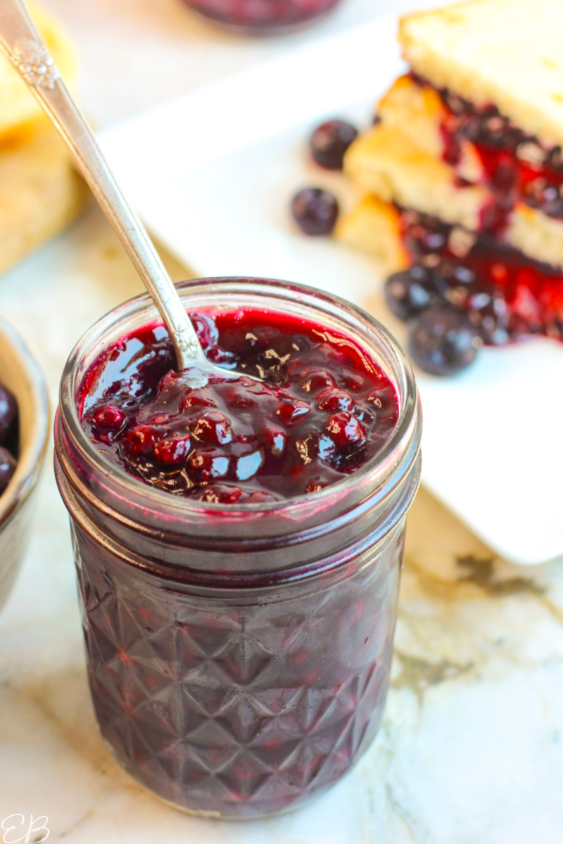 spoon in blueberry jam jar with sandwich in the background