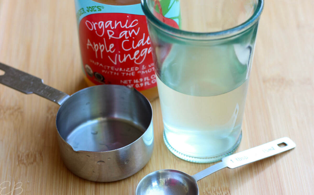 glass of water and acv with bottle of apple cider vinegar and measuring tools