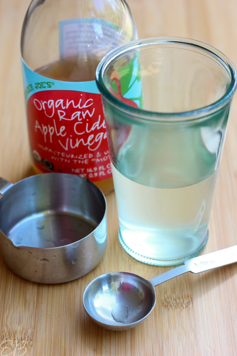 glass of water and acv with bottle of apple cider vinegar and measuring tools