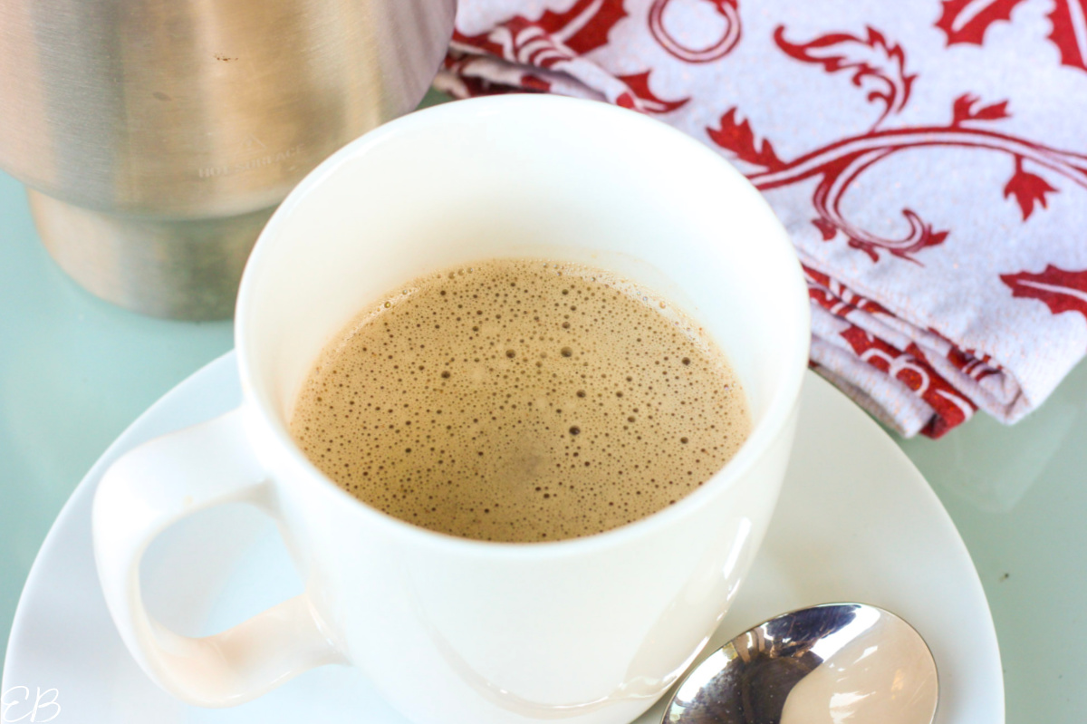hot carob drink in white mug with milk frother behind