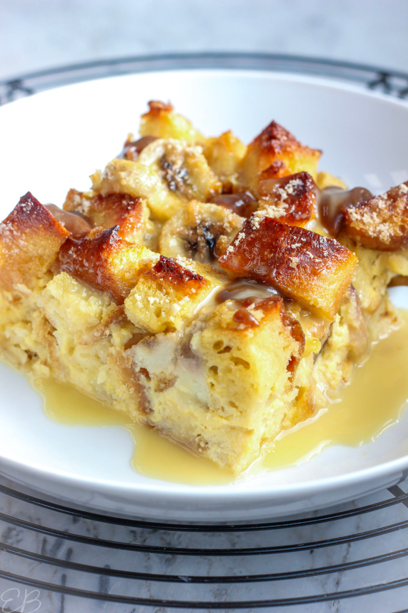 close up photo of banana bread pudding in white dish with warm vanilla custard and caramel sauce