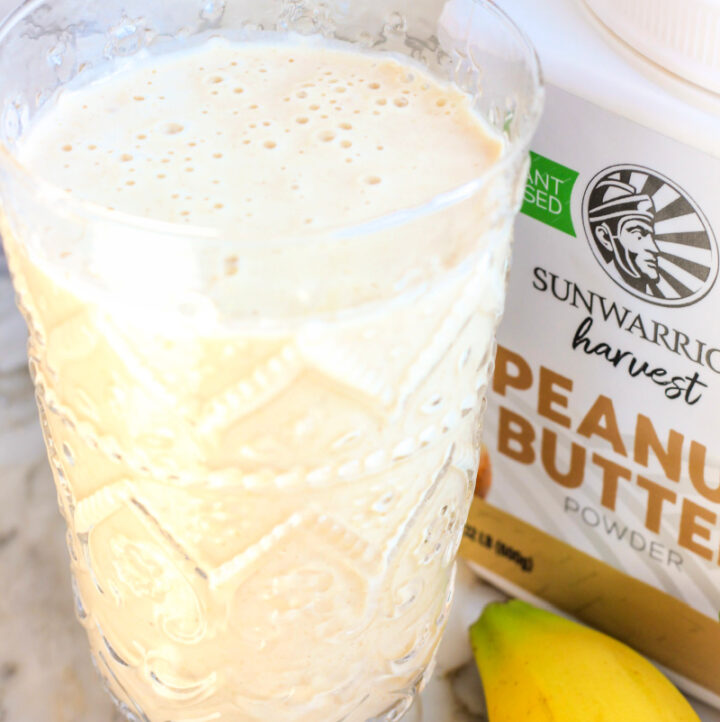 up close photo of peanut butter banana oat smoothie for weight loss in tall clear glass, with pb powder canister in background