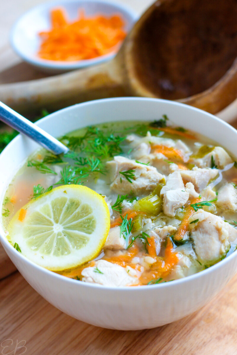 greek lemon chicken soup in white bowl, with fresh lemon slice on top