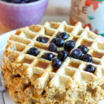 up close photo of gluten free high protein waffles on white plate with syrup and berries