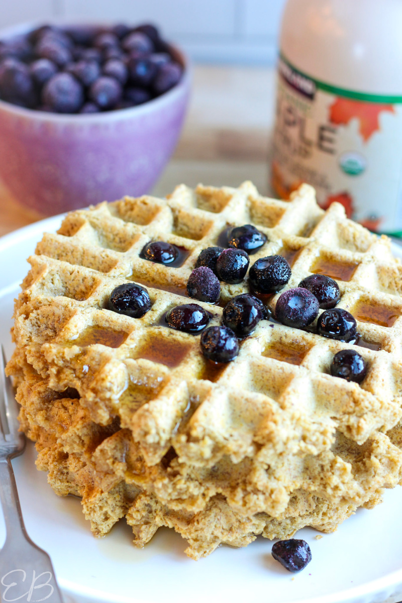 up close photo of gluten free high protein waffles on white plate with syrup and berries
