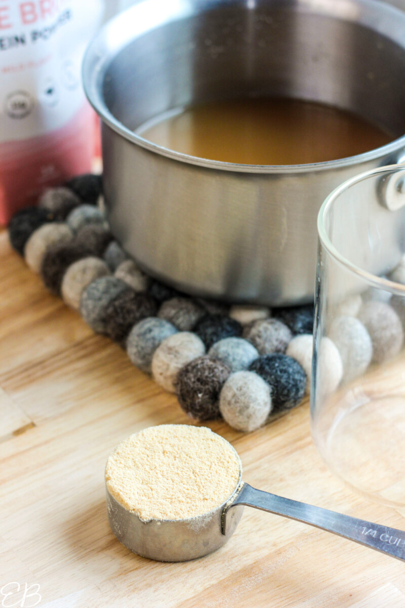 grass fed bouillon powder in measuring cup, with it made into broth in a saucepan in the background
