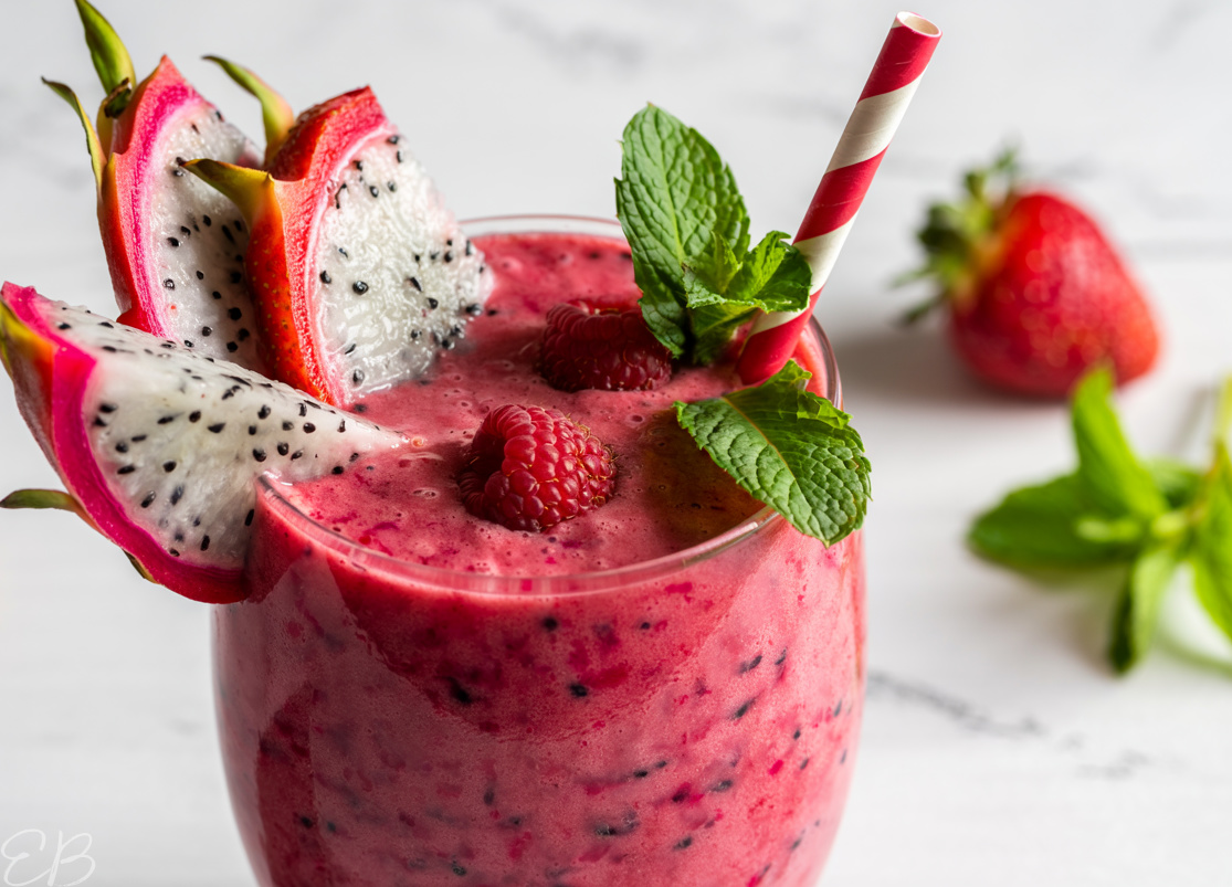 dragon fruit smoothie in glass with slices of dragon fruit and raspberries garnishing