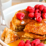 gluten free vegan Oat Flour Pancakes cut into with maple syrup and raspberries on top
