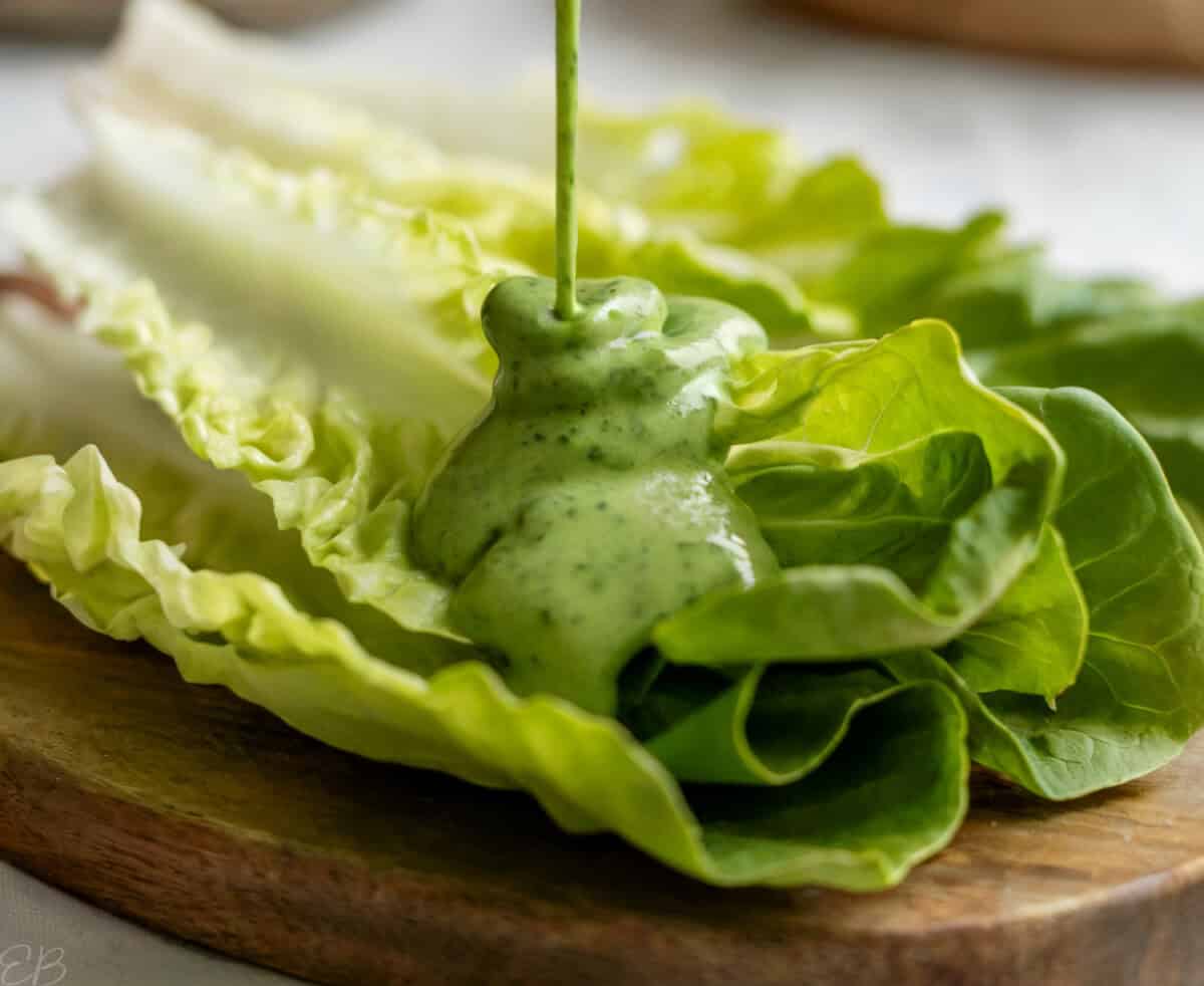 close up photo of creamy tarragon hemp dressing being poured onto romaine lettuce