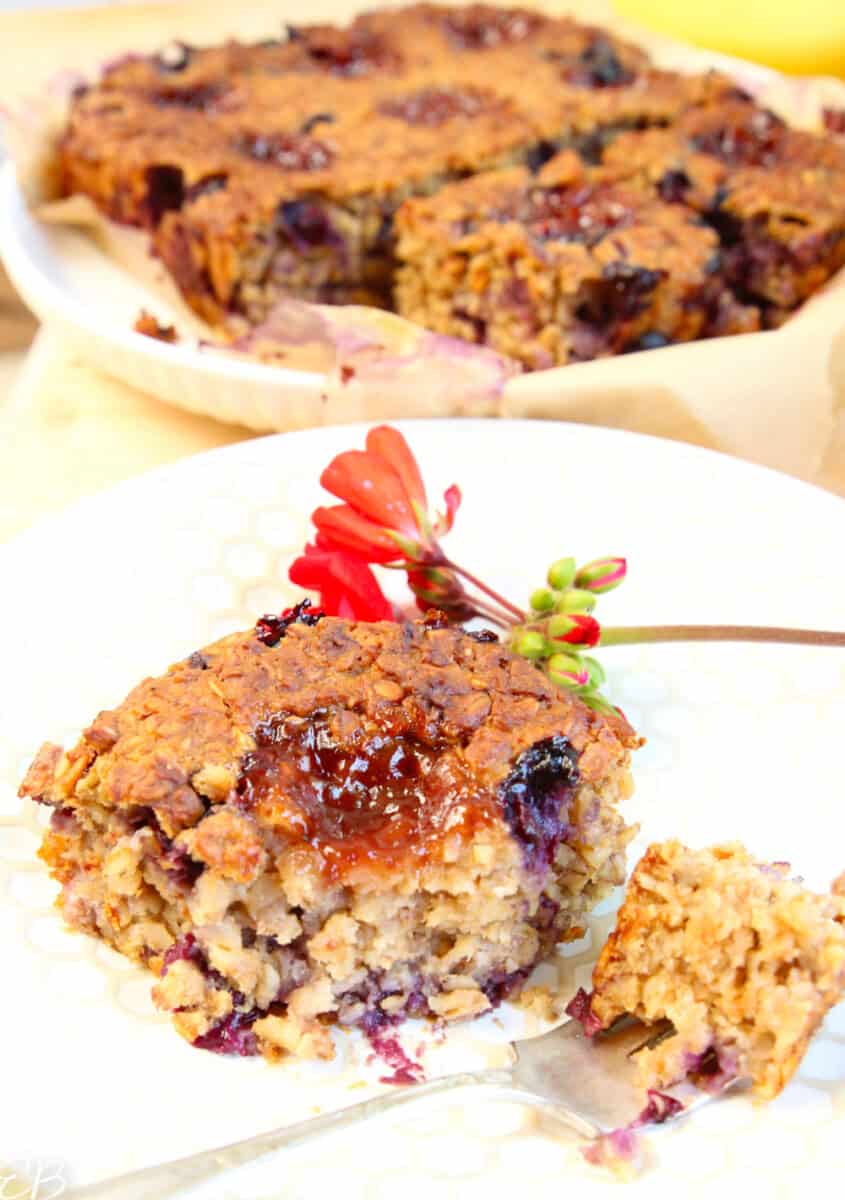 close up square of baked peanut butter and jelly oatmeal with whole vegan breakfast casserole in background