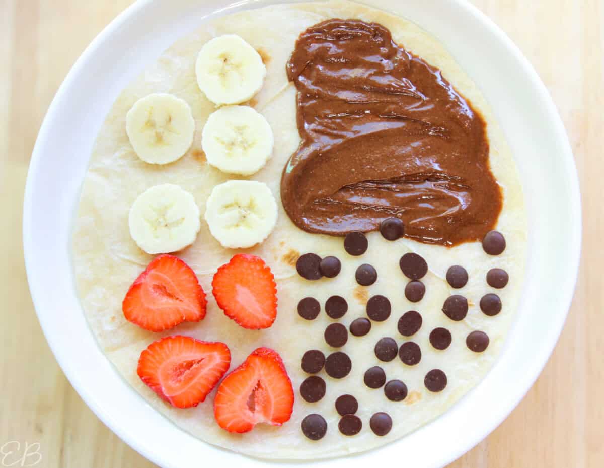 overhead view of strawberry slices, banana slices, chocolate spread, and carob chips sandwich wrap for kids' lunches, not folded yet