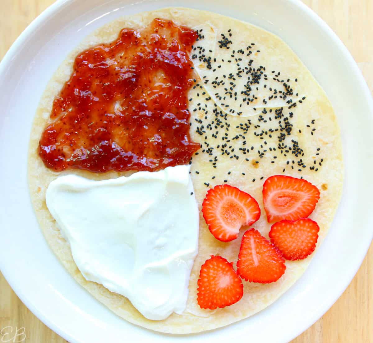 overhead view of Greek yogurt, strawberry jam, chia seeds or basil seeds and strawberries sandwich wrap for kids' lunches, not folded yet