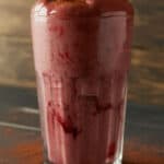 cacao beet smoothie for constipation in tall clear glass with cocoa powder dusted around the base