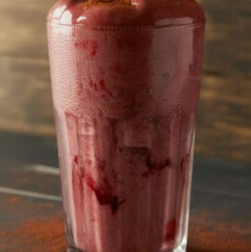 cacao beet smoothie for constipation in tall clear glass with cocoa powder dusted around the base