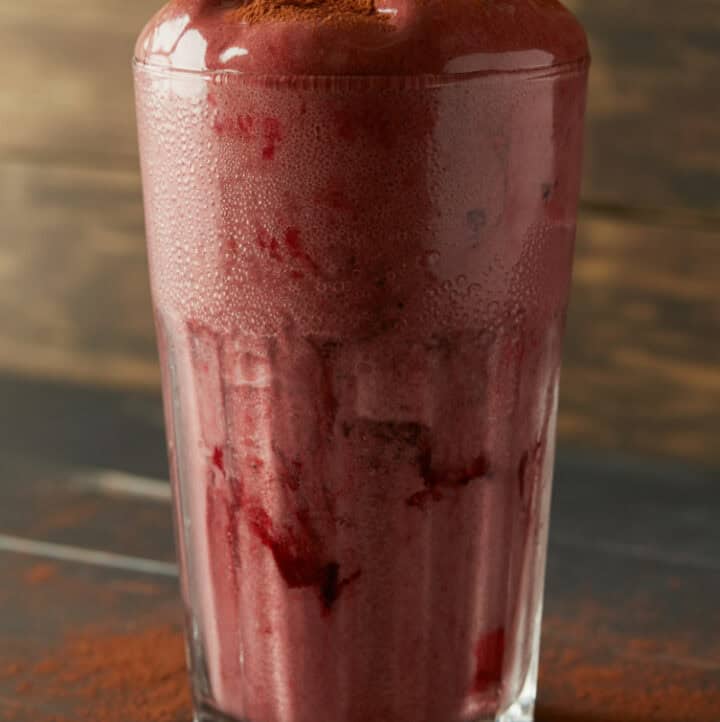 cacao beet smoothie for constipation in tall clear glass with cocoa powder dusted around the base