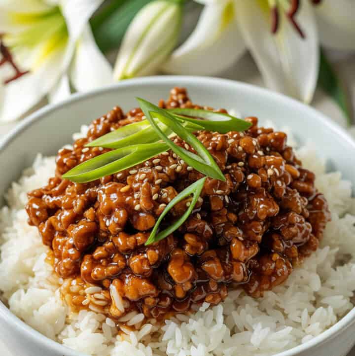 Asian Beef Bowl served with white rice, and lillies in the background