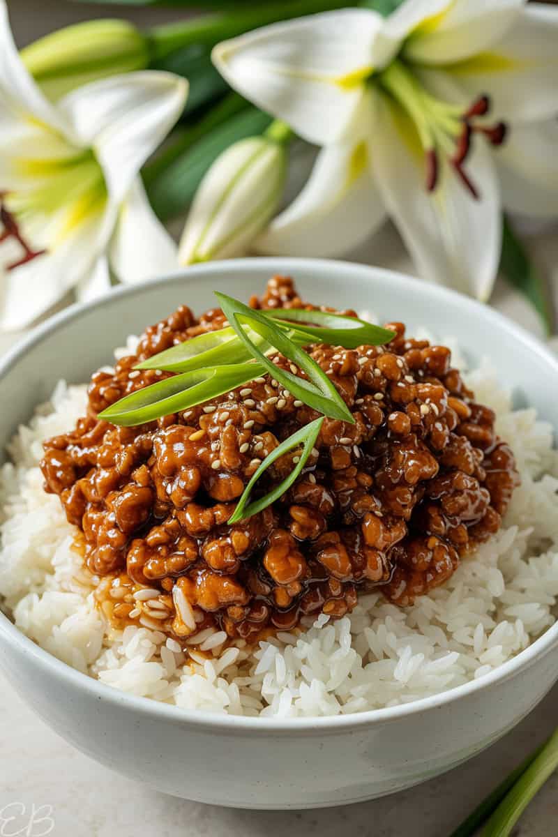 Asian Beef Bowl served with white rice, and lillies in the background
