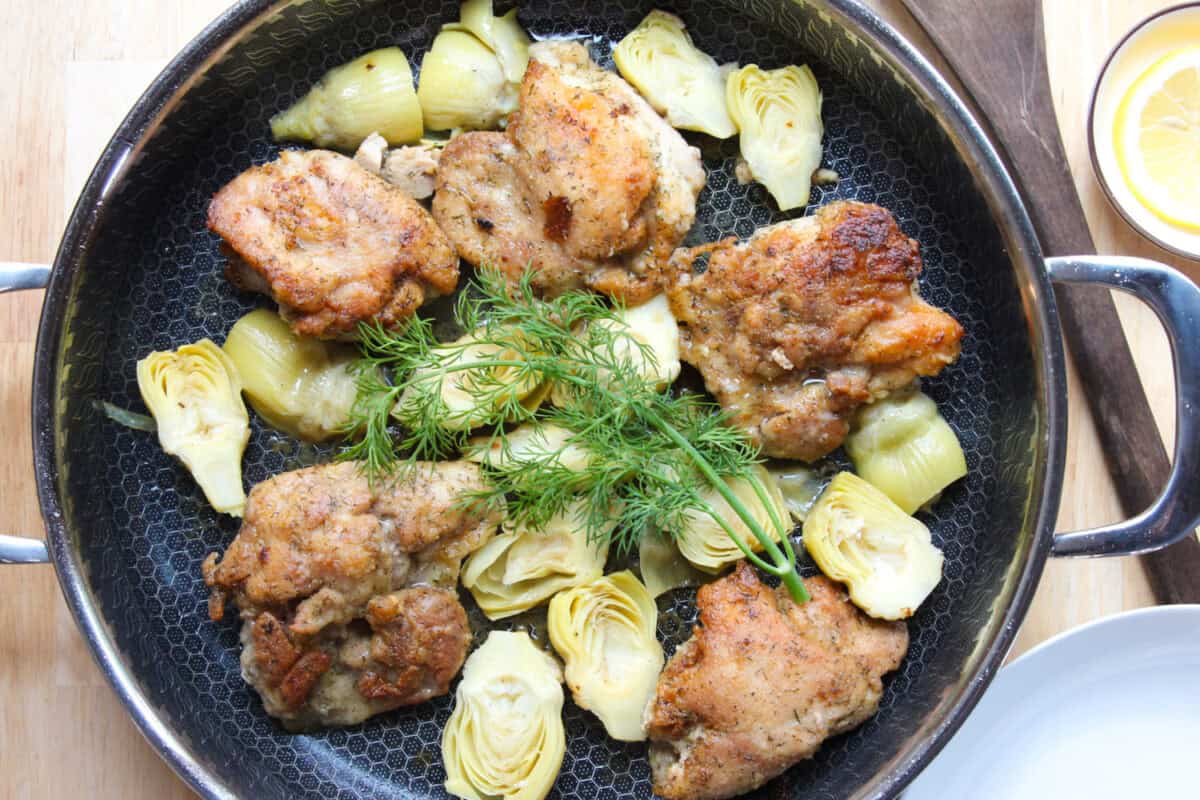 overhead view of lemon chicken skillet with artichokes topped with fresh dill