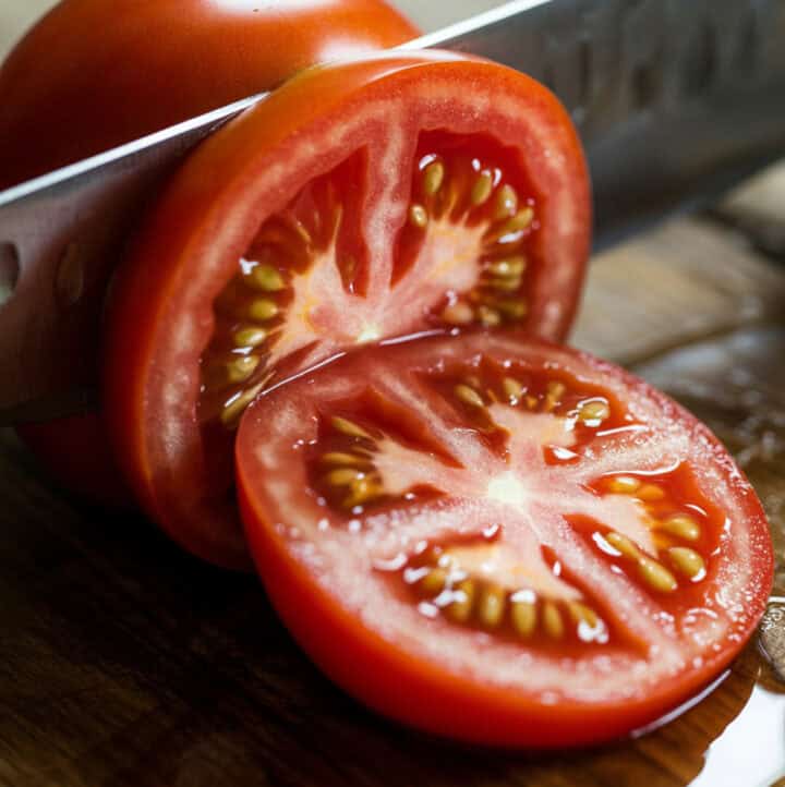 a juicy tomato being sliced on cutting board