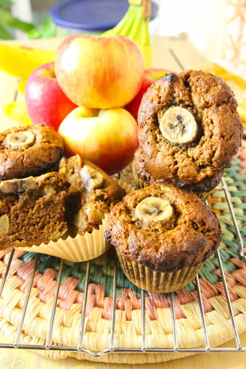 brightly lit apple spice banana muffins on cooling rack with fresh apples