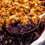 gluten free blueberry crisp with oats being served from a white casserole dish