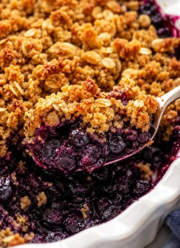 gluten free blueberry crisp with oats being served from a white casserole dish