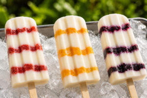 vegan cheesecake popsicles on ice in 3 flavors: Strawberry, Peach and Blueberry