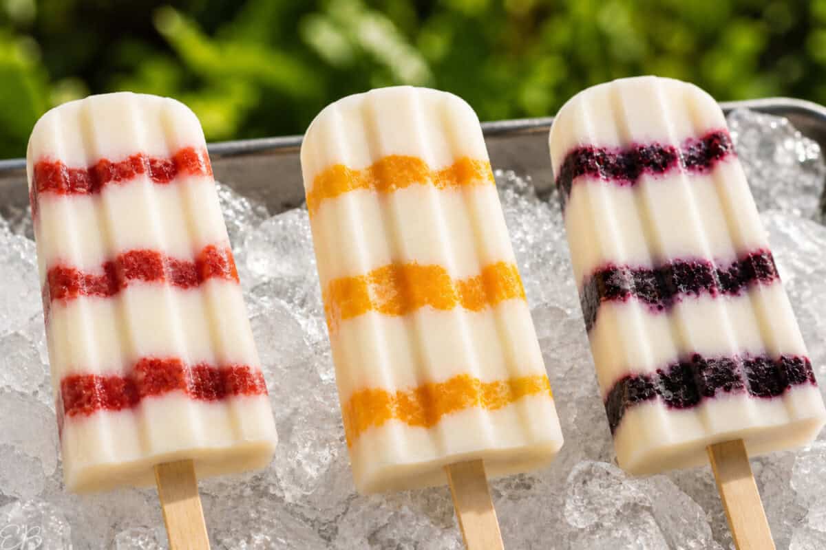 vegan cheesecake popsicles on ice in 3 flavors: Strawberry, Peach and Blueberry