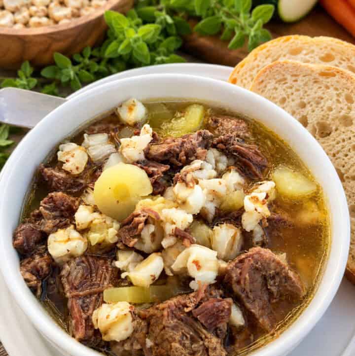 side angle view of rich beef posole stew with hominy, served with bread