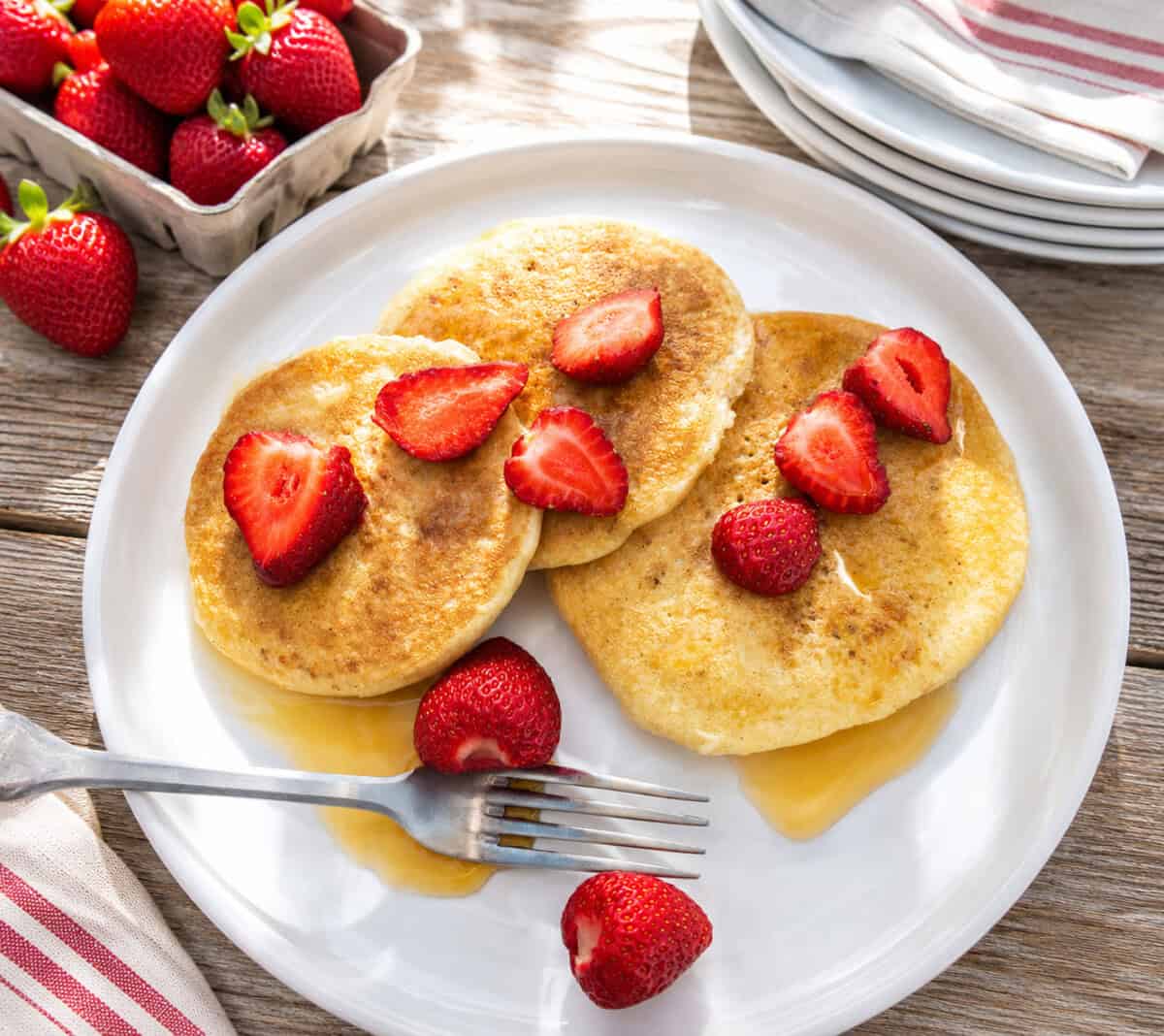 overhead view of sourdough pancakes served on white plate with strawberries